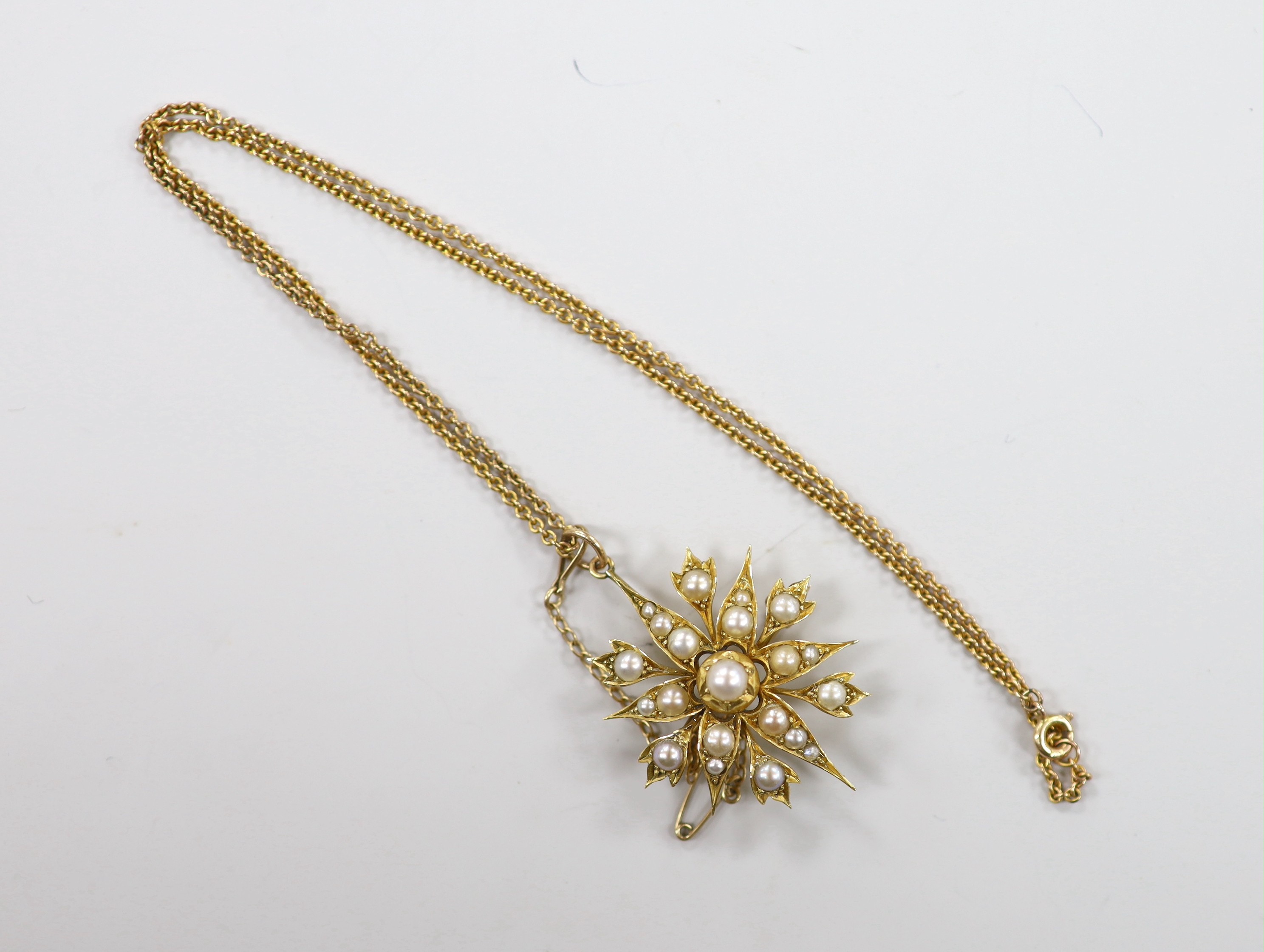 An Edwardian yellow metal and split pearl cluster set starburst pendant brooch, 37mm, on a later 9ct chain, 40cm, gross weight 9.6 grams.